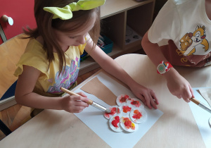Dziewczynka i chłopiec robią prace plastyczną – jesienne drzewo. Malują farbą koronę drzewa zrobioną z płatków kosmetycznych.