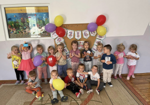 Dzieci pozują do wspólnego zdjęcia na tle dekoracji z okazji Dnia Przedszkolaka.