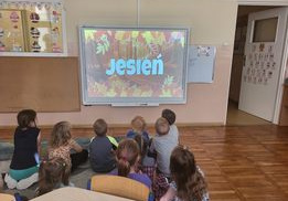 Dzieci z grupy Smerfy siedzą na dywanie i oglądają film edukacyjny "Kazio i jesień ".