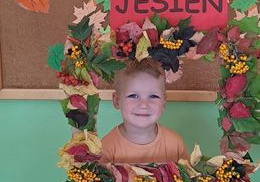 Chłopiec z grupy Misie pozuje do zdjęcia w ramce wykonanej z liści oraz jarzębiny z napisem jesień.
