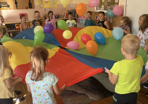 Dzieci z grupy „Smerfy” podczas zabawy chustą animacyjną i balonami.