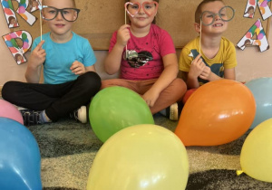 Troje dzieci pozuje do zdjęcia, trzymając w ręku rekwizyty okularów.