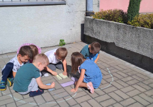Dzieci na tarasie w ogródku przedszkolnym kolorują kredą narysowany szablon jabłka.