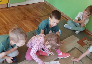 Dziewczynka układa obrazek z trzech elementów, reszta dzieci siedzi na dywanie.