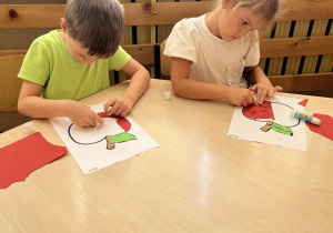 Chłopczyk i dziewczynka wyklejają jabłko kolorowym papierem.