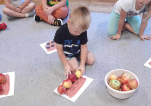 Chłopiec układa odpowiednią ilość jabłek na obrazku koszyka.