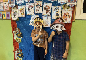 Chłopcy stoją na tle dekoracji trzymając przy twarzach maski postaci z bajek i pozują do zdjęcia.