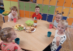 Dzieci przy stoliku częstują się smakołykami, które przygotowali rodzice na Dzień Chłopaka.