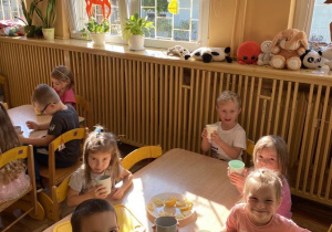 Dzieci siedzą przy stoliku i piją sok z cytryny.