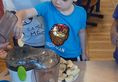 Chłopiec w niebieskiej bluzce z grupy Żabki wrzuca jabłko do sokowirówki, z której wypływa sok jabłkowy.