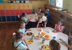 Dzieci siedzą przy stolikach i częstują się przygotowanymi łakociami.