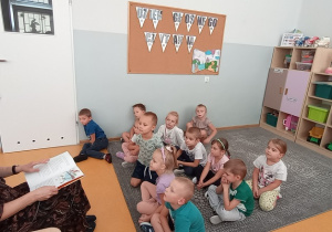Dzieci z grupy Liski siedzą na dywanie i słuchają opowiadania czytanego przez Panią logopedę.