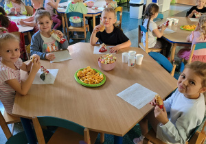 Trzy dziewczynki i chłopiec siedzą przy stoliku i jedzą rogaliki.