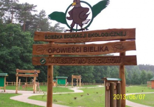 Zdjęcie przedstawia wejście na ścieżkę edukacji przyrodniczej w Nadleśnictwie Bełchatów. Wejście tworzy drewniany łuk z symbolem ptaka bielika.