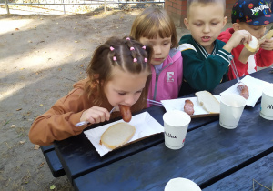 Troje dzieci siedzą przy stole, jedząc kiełbaski z grilla.