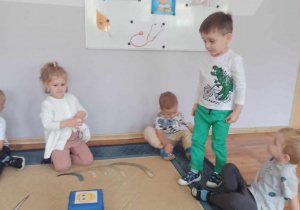 Dzieci grają na dywanie kostką z emotkami.