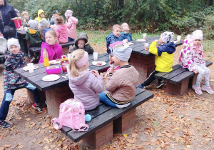 Dzieci z różnych grup jedzące upieczoną na grillu kiełbaskę.