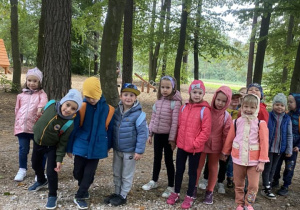 Dzieci z grupy Odkrywcy pozują do zdjęcia na tle lasu.