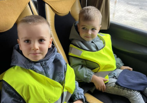 Chłopcy siedzą uśmiechnięci na fotelach w autobusie ubrani w kamizelki odblaskowe