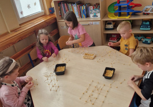 Dzieci siedzą przy stoliku i budują konstrukcje, przy użyciu ciecierzycy i wykałaczek.