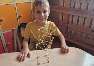 Chłopiec siedzi przy stoliku i prezentuje swoją konstrukcję.
