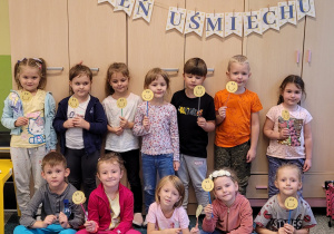 Wspólna fotografia na tle napisu Dzień Uśmiechu. Dzieci trzymają tabliczki z uśmiechami.