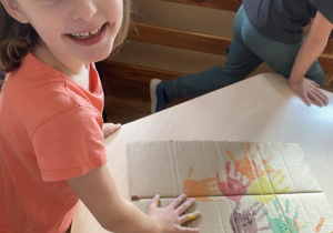 Dziewczynka odbija swoją dłoń pomalowaną farbą na pracy plastycznej.
