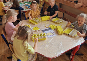 Dzieci siedzą przy stolikach i malują farbami swoje wytłaczanki.