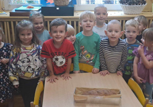 Dzieci pozują do zdjęcia na stoliku leży blaszka z upieczonym chlebem.