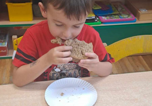 Chłopiec siedzi przy stoliku i je chleb.