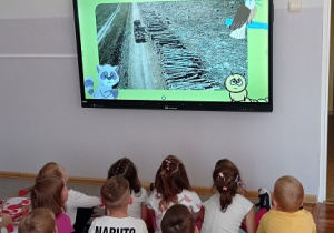 Wykorzystanie monitora podczas zajęć w Dniu Drzewa- Dzieci siedzą na dywanie, oglądają film dydaktyczny dotyczący drzewa.